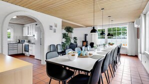 Eine moderne Küche mit weißen Schränken, ein Essbereich mit einem langen Tisch und Stühlen sowie eine Holzbalkendecke.