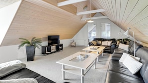 Ein stilvolles Loft-Wohnzimmer mit schrägverdachter Decke, einem schwarzen Ledersofa, einem weißen Couchtisch und einem Fernseher.