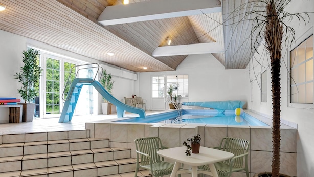 Ein Poolbereich mit Rutsche, Stufen zum Pool und einer Sitzgelegenheit mit Stühlen und Tisch.