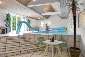 Ein Poolbereich mit Rutsche, Stufen zum Pool und einer Sitzgelegenheit mit Stühlen und Tisch.