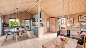 Een ruime woonkamer met houten plafond, een eettafel met stoelen, een bank en een keuken met raam.