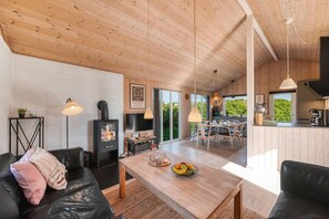 A modern living room with a fireplace, wooden ceiling, and a dining area with natural light. - Lovely holiday home with 6-person outdoor hot tub, close to the North Sea and. (Ringkøbing)
