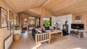 Een ruime woonkamer met houten plafond, een bank, een televisie en een open haard.