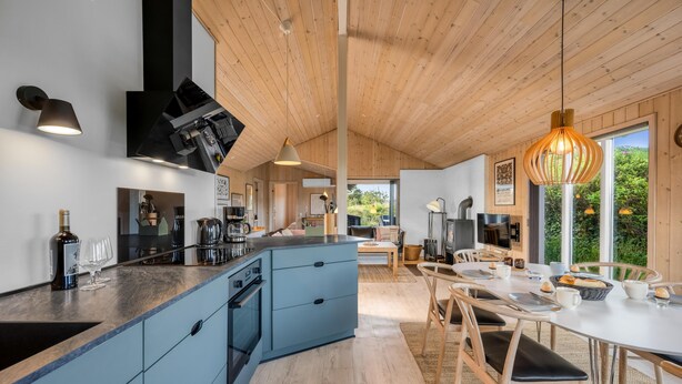 Een moderne keuken met een blauw kookeiland, een houten plafond en een eethoek met een witte tafel en stoelen.