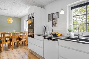 A modern kitchen with white cabinetry, a black countertop, and a window with a view of trees. - Large pool house in Husby with sleeping space for 18 people. (Ulfborg)