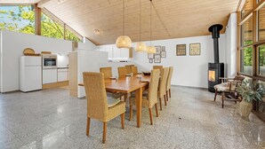 Eine moderne Küche mit weißen Schränken, ein Essbereich mit Korbstühlen, einem großen Holztisch und einem Kaminofen.