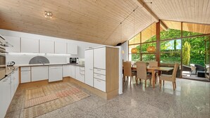 Eine moderne Küche mit weißen Schränken, ein Essbereich mit Tisch und Stühlen sowie große Fenster mit Blick auf Grünflächen.