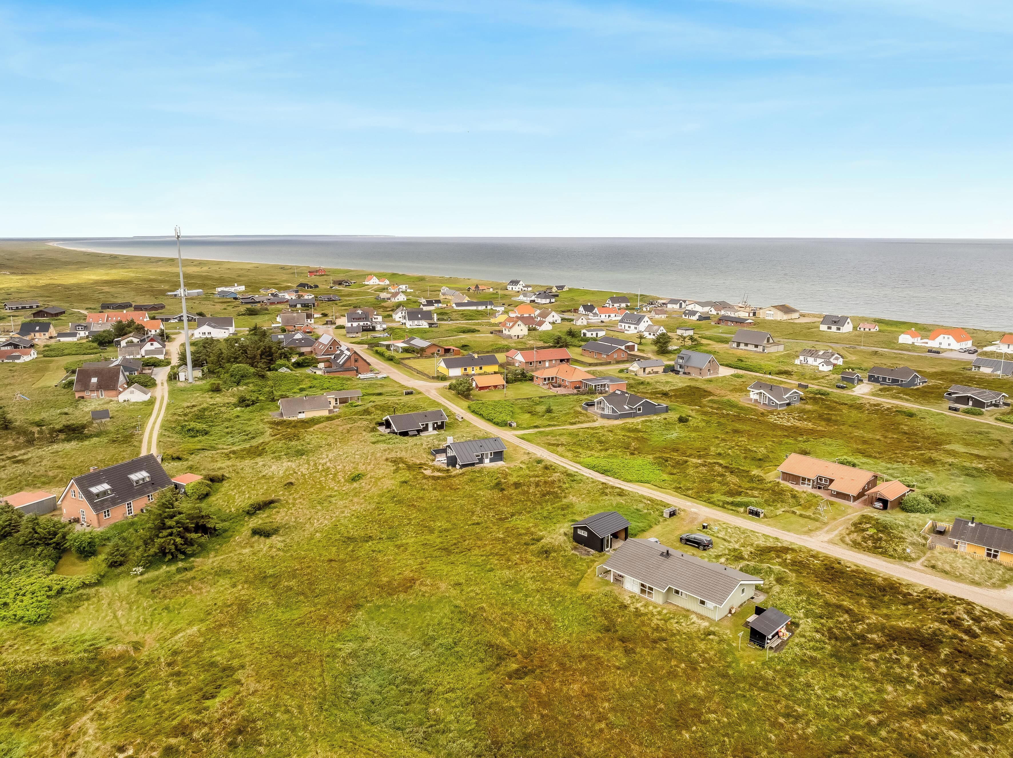 An aerial view of a coastal village with houses, roads, and a lighthouse.