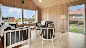 Een kamer met houten wanden, een bank, een stoel, een tafel en grote ramen.