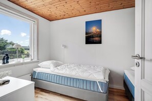 Ein Schlafzimmer mit Bett, Fenster mit Blick, einem Gemälde an der Wand und einem weißen Nachttisch.
