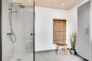Ein modernes Badezimmer mit einer Glaskabine zur Dusche, einer Holzbank und einem Blumentopf.