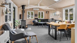 Ein gemütlicher Innenraum mit Holzbalkendecke, einer Couch, einem Esstisch und einem Kamin.