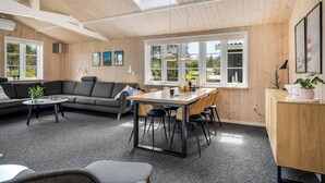 Ein gemütliches Zimmer mit Holzbalkendecke, einer Couch, einem Esstisch mit Stühlen und einem großen Fenster.