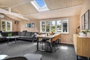 A cozy room with a wooden ceiling, a sofa, a dining table with chairs, and a large window. - Lovely renovated holiday home, with large enclosed terrace, in Vorupør by the. (Thisted)