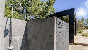A modern outdoor shower with a metal rain showerhead, a concrete wall with a marble-like pattern, and a wooden deck.