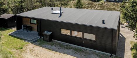 A modern, single-story building with a flat roof, large windows, and a small patio area.
