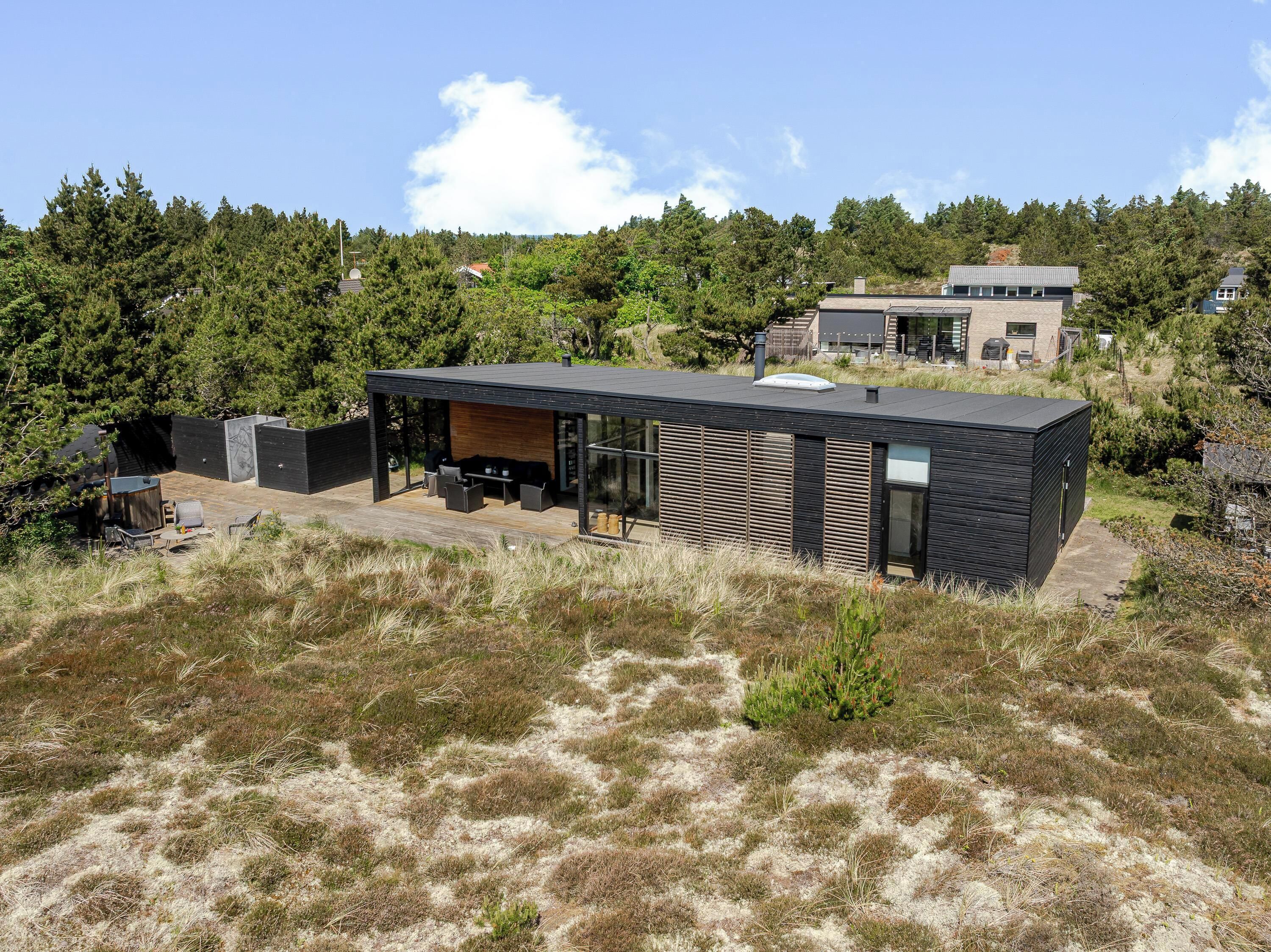 Une maison moderne dotée d’un patio, d’un garage et située devant une colline boisée.