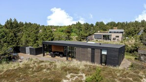 A modern house with a patio, a garage, and a forested hill in the background.