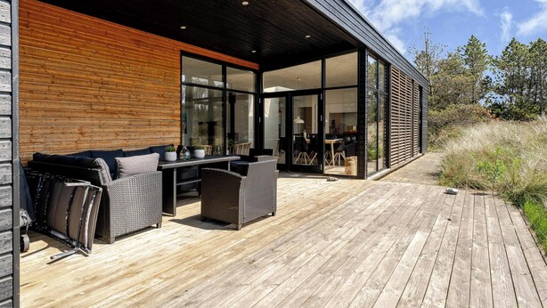A modern outdoor patio with wicker furniture, a wooden deck, and a glass-enclosed room.