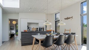 A modern kitchen with a dining area, large windows, and a view of the outdoors.