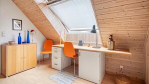 A compact, modern kitchen with wooden cabinetry, a small refrigerator, and a dining area with a single orange chair.
