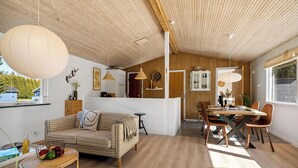 Een modern interieur met een houten plafond, een eethoek met een houten tafel en stoelen, een bank en een rieten bijzettafeltje met fruit.