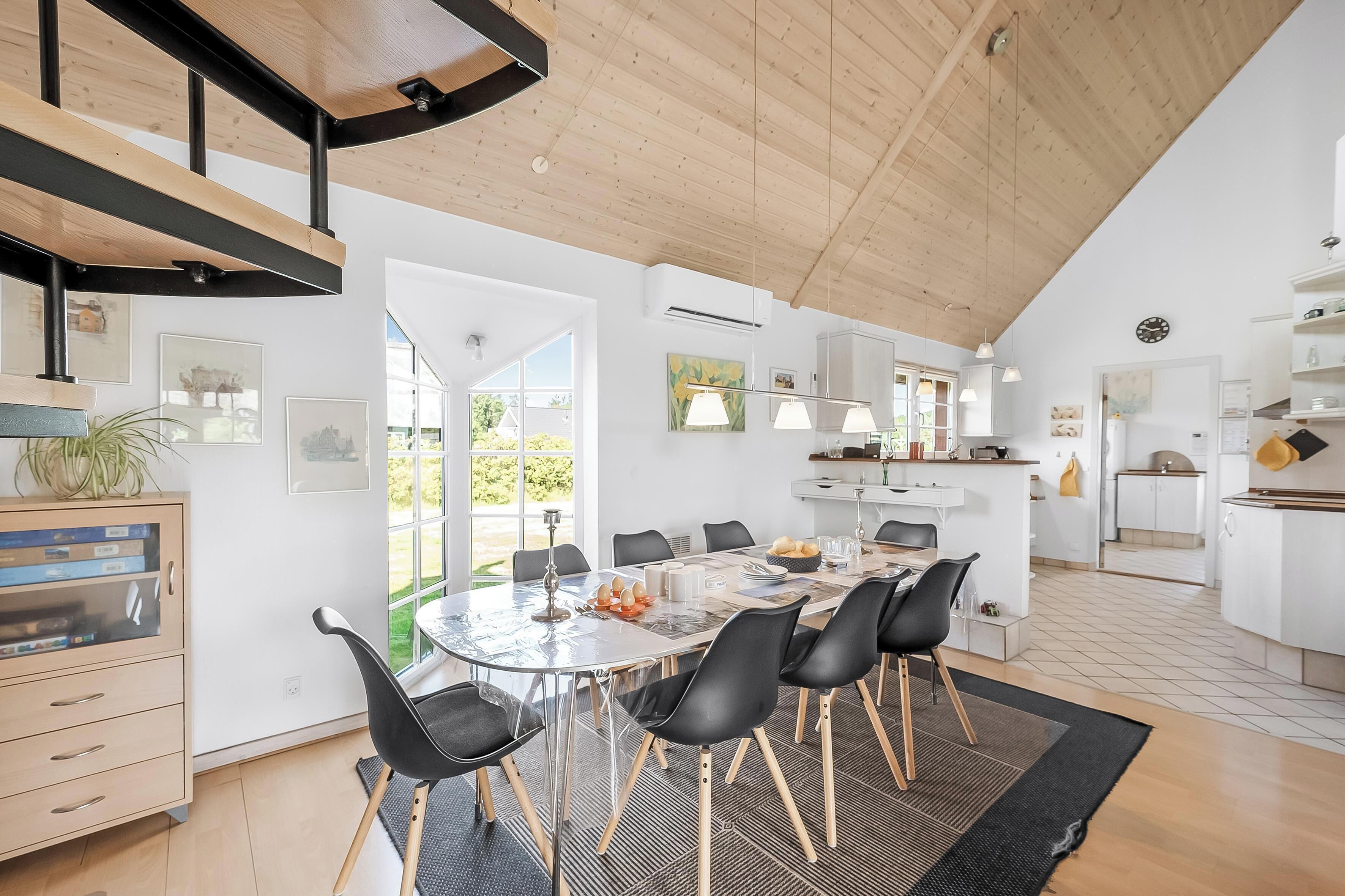 Een moderne keuken met witte kasten, een centraal eiland en een eetgedeelte met een glazen tafel en zwarte stoelen.