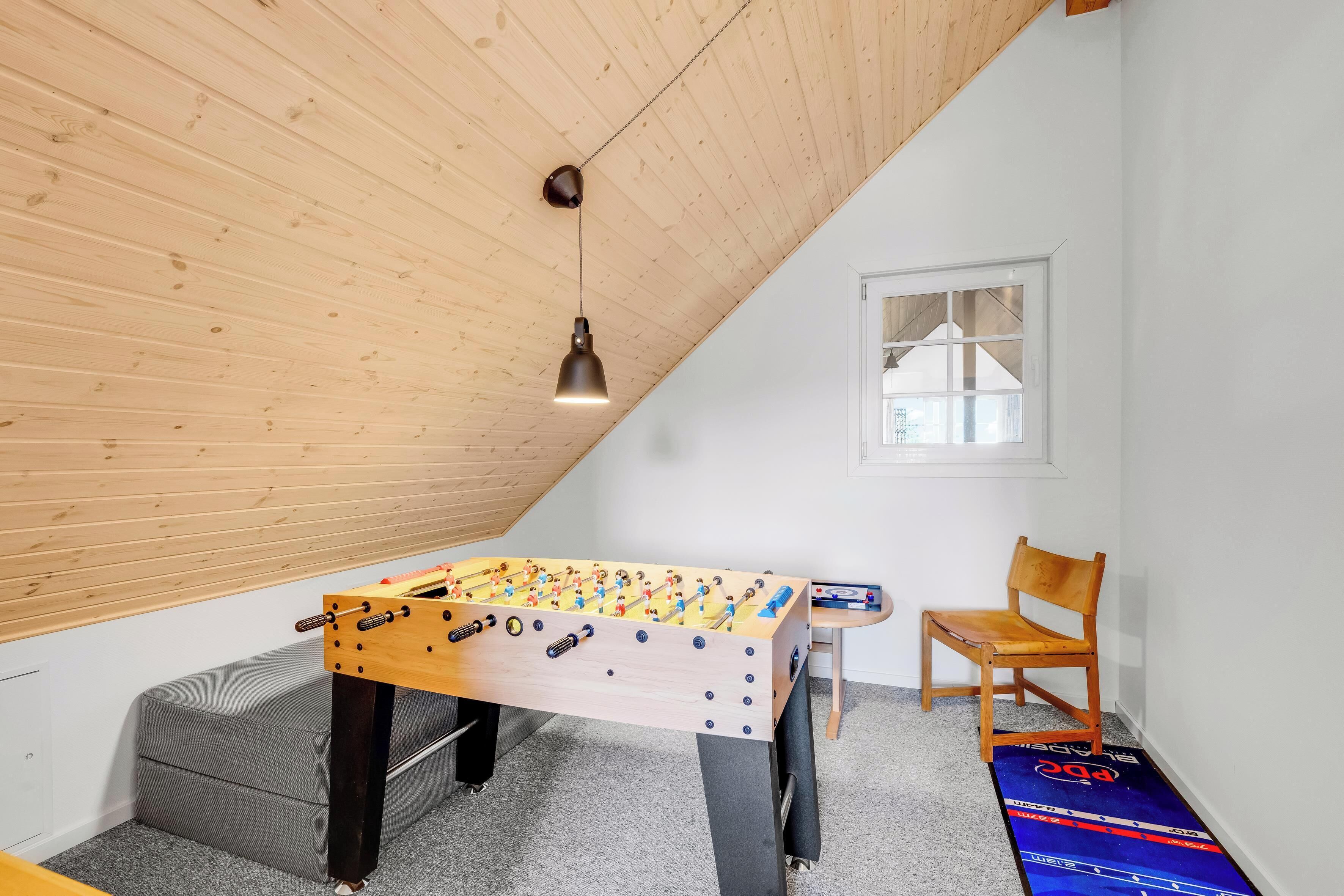 Ein Zimmer mit einem Tischkicker, einem Holzstuhl und einem Fenster.