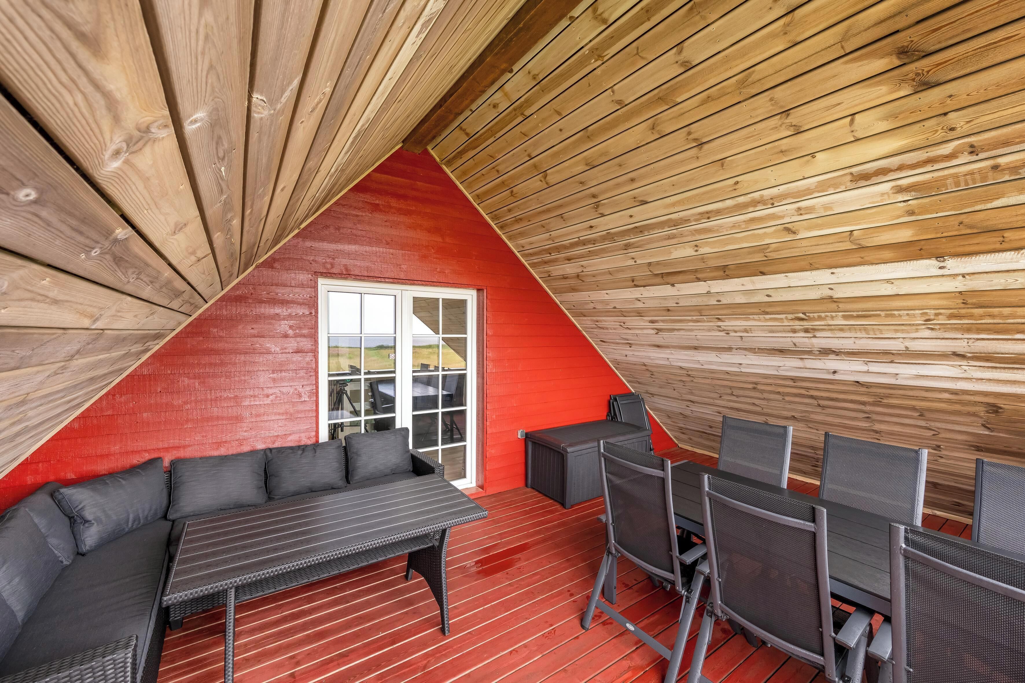 Un cuarto acogedor con forma triangular, una pared roja, un ventanal grande y una zona de comedor con una mesa y sillas.