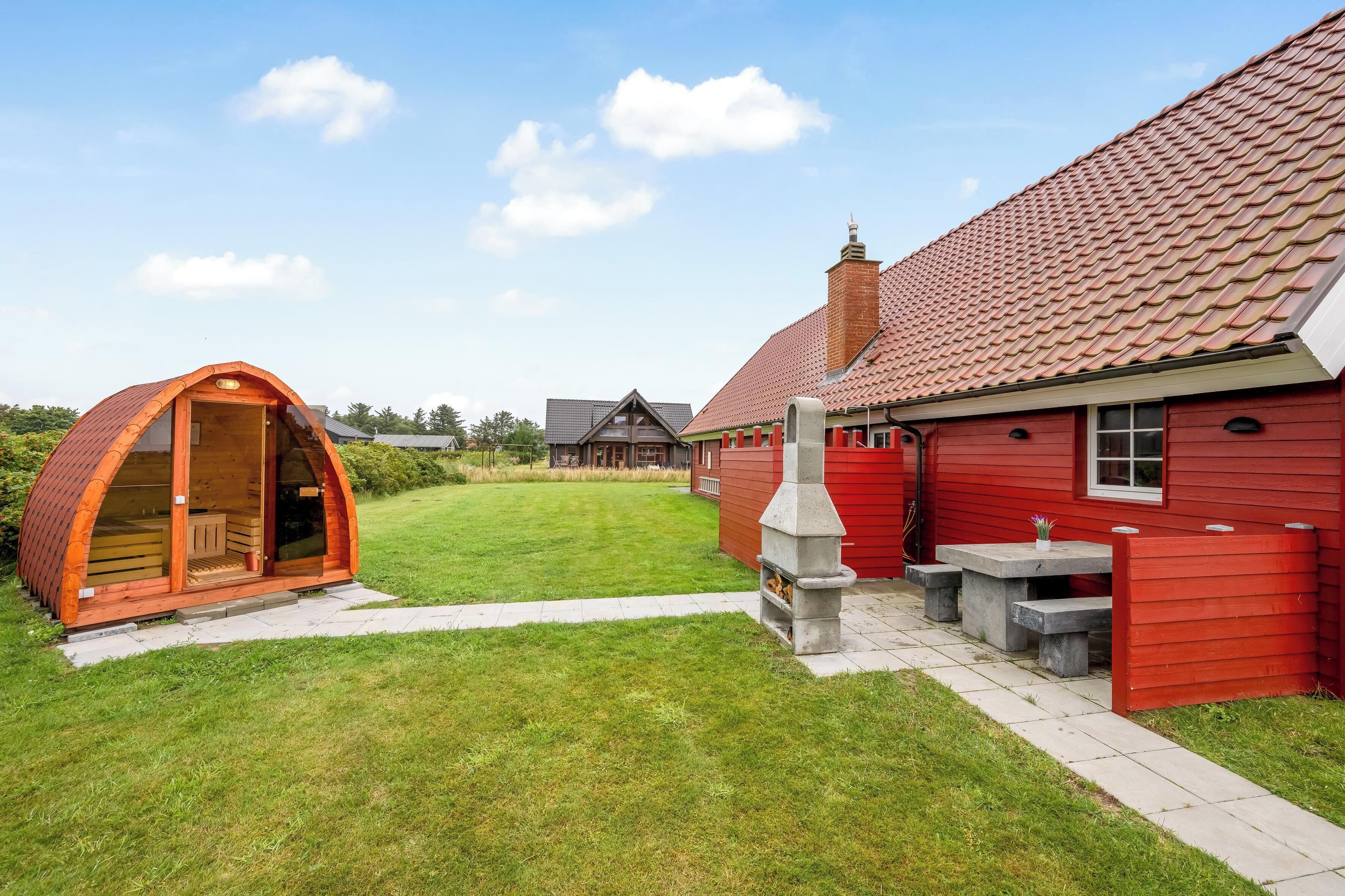 Un bâtiment rouge avec une cheminée en pierre, un banc en pierre et une petite structure en bois dotée d’une porte en verre.