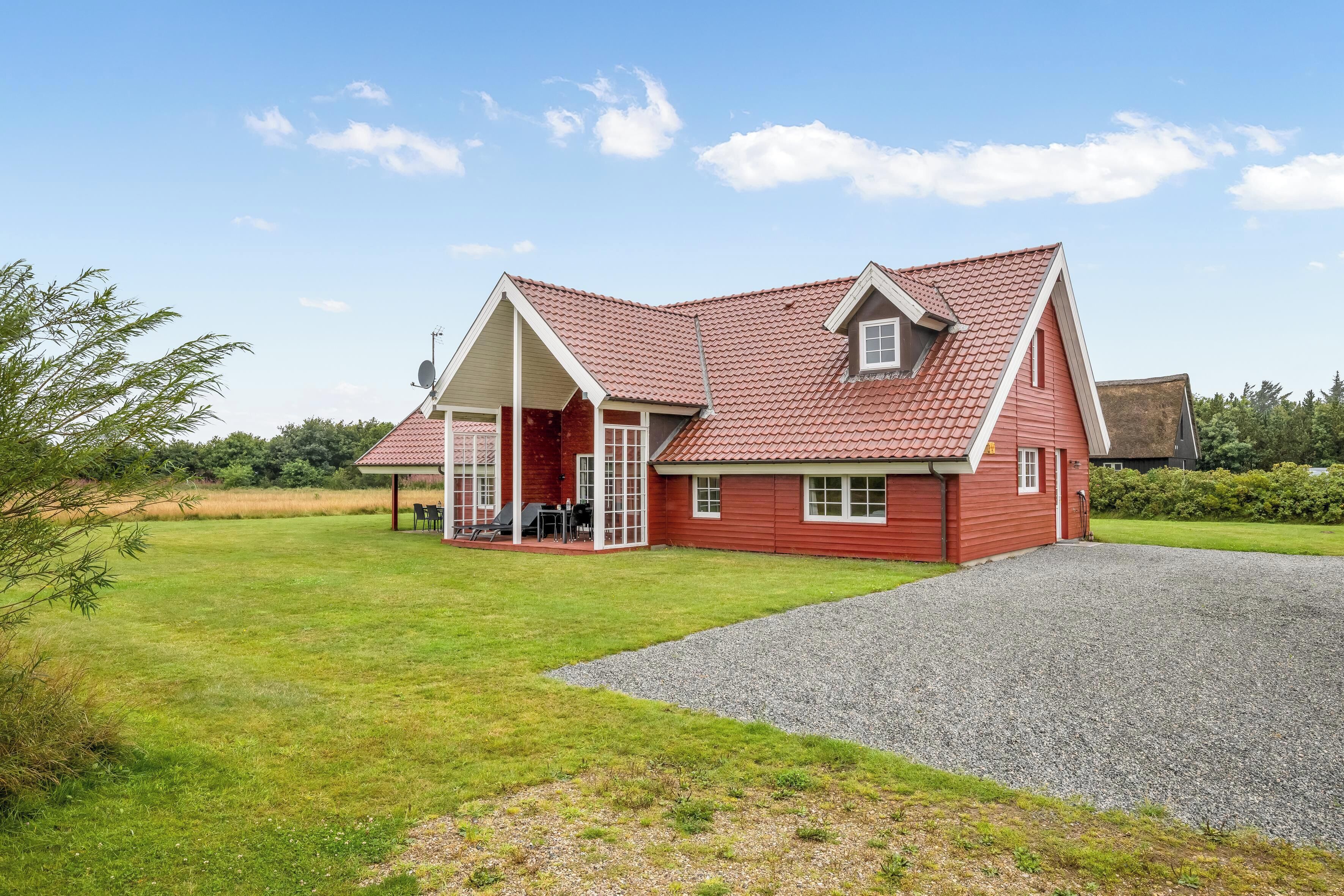 A red house with a gravel driveway and a grassy lawn.