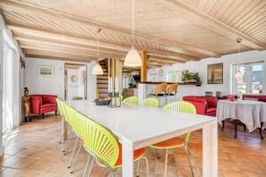 A spacious dining area with a white table and yellow chairs, wooden ceiling beams, and a red sofa in the background. - Lovely holiday home with wilderness bath and outdoor sauna, centrally located. (Thisted)