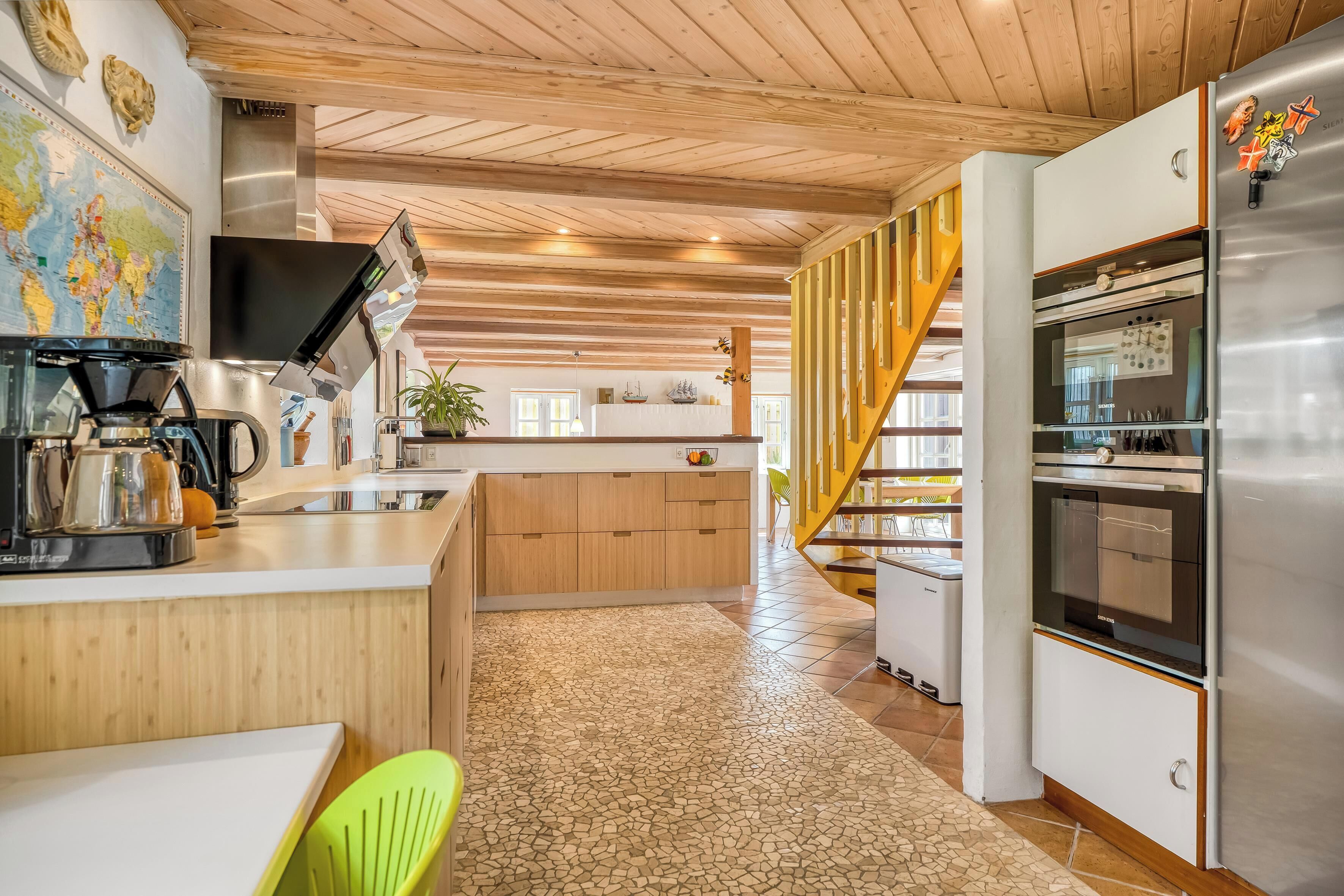 Una cocina moderna con una isla central, techo de madera y un refrigerador de acero inoxidable.
