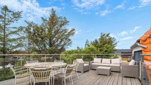 A wooden deck with outdoor furniture, including a round table and chairs, and a sofa set. - Lovely holiday home with wilderness bath and outdoor sauna, centrally located. (Thisted)