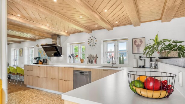 A modern kitchen with wooden beams, a central island, a sink, and a fruit bowl. - Lovely holiday home with wilderness bath and outdoor sauna, centrally located. (Thisted)