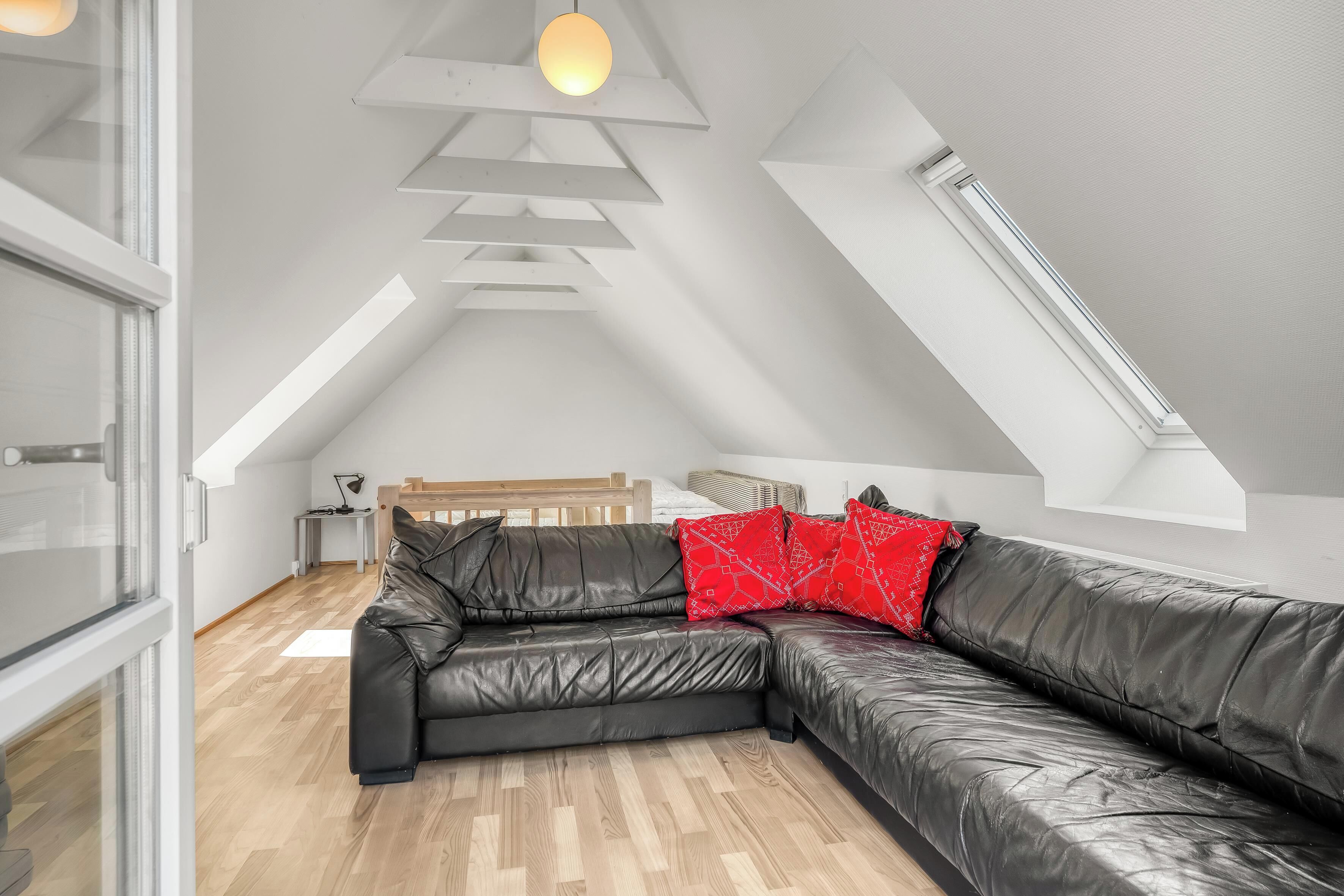 Un dormitori modern tipus loft amb un sofà seccional de cuir negre, un panell de fusta al capçal i un finestral de sostre.