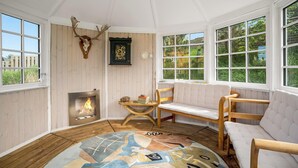 A room with a fireplace, wooden furniture, a rug, and a deer skull on the wall. - Lovely holiday home with wilderness bath and outdoor sauna, centrally located. (Thisted)