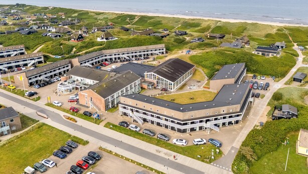 Vista aerea di un hotel costiero con diversi edifici, aree di parcheggio e una spiaggia sullo sfondo.