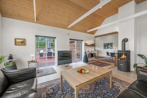 Amplia sala de estar con techo de madera, televisión, mesa de comedor con fruta y estufa de leña.