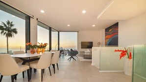 Un comedor moderno con vista al océano, un televisor de pantalla plana y un panel de vidrio con plantas decorativas.