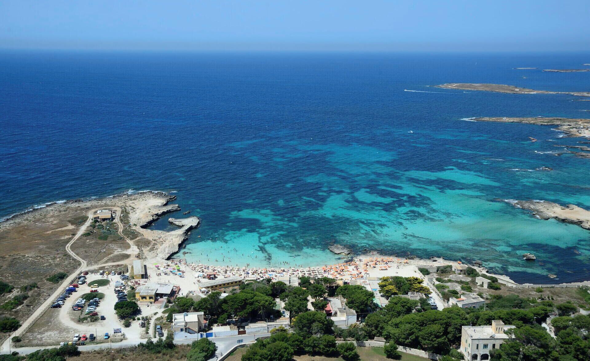Vista aérea de un pueblo costero con playa, aguas azul turquesa y una combinación de edificios residenciales y comerciales.