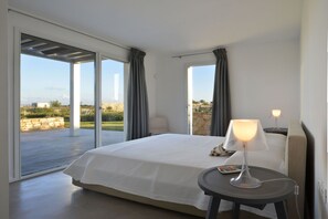 A bedroom with a bed, a bedside table with a lamp, and a view of the outdoors.