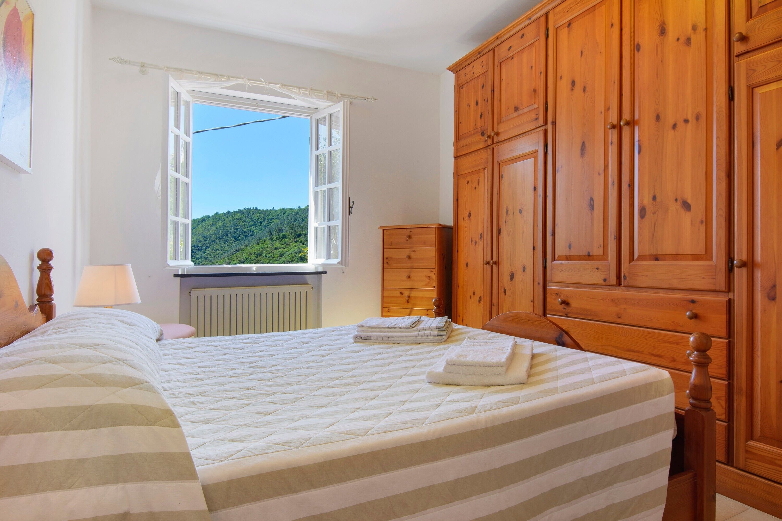 Ein Schlafzimmer mit einem Bett, einem Fenster mit Blick auf Grünflächen, einem Holzschrank und einer Heizung.