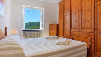 Ein Schlafzimmer mit einem Bett, einem Fenster mit Blick auf Grünflächen, einem Holzschrank und einer Heizung.