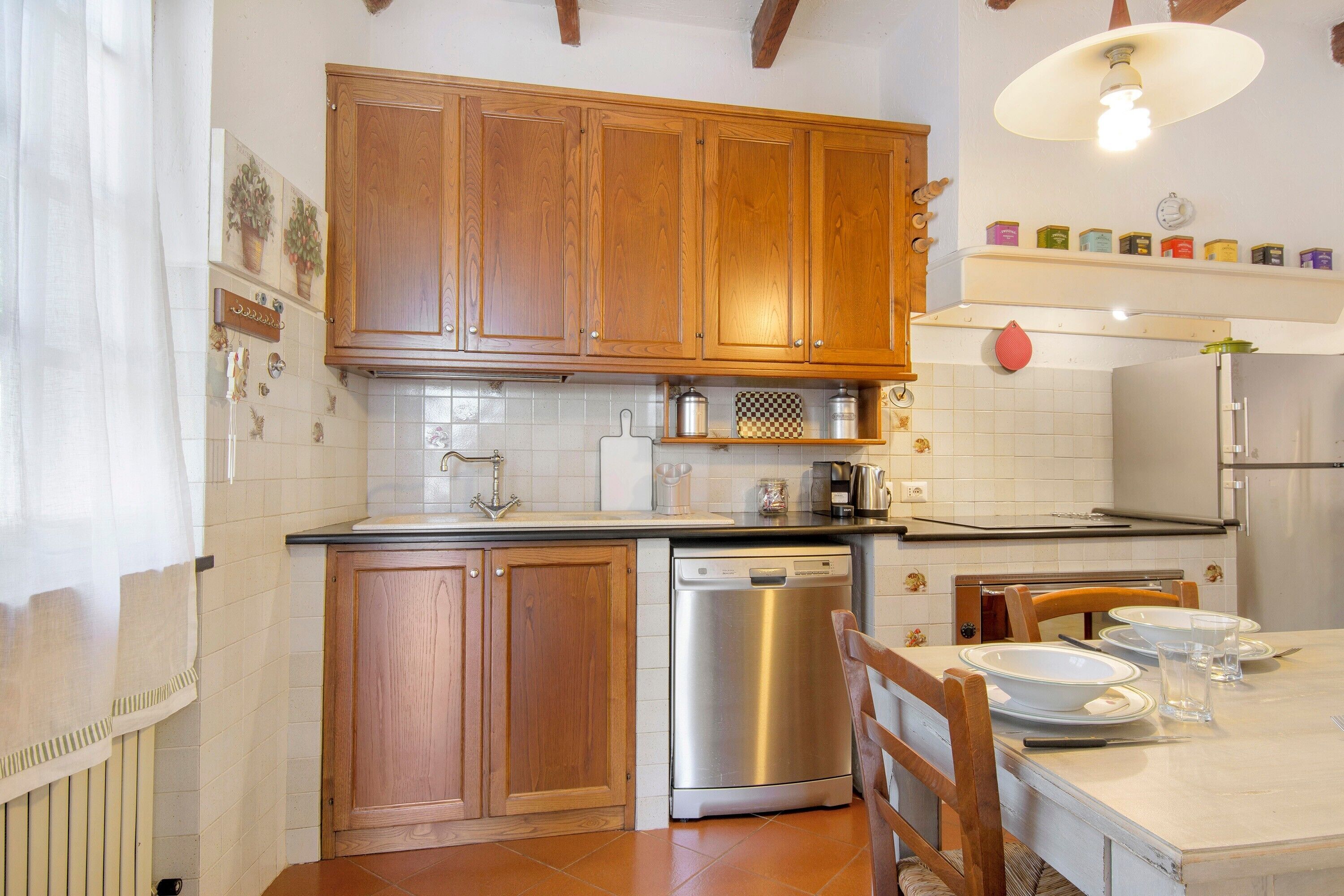 A kitchen with wooden cabinets, a dishwasher, a tiled backsplash, and a dining table set with plates and glasses.