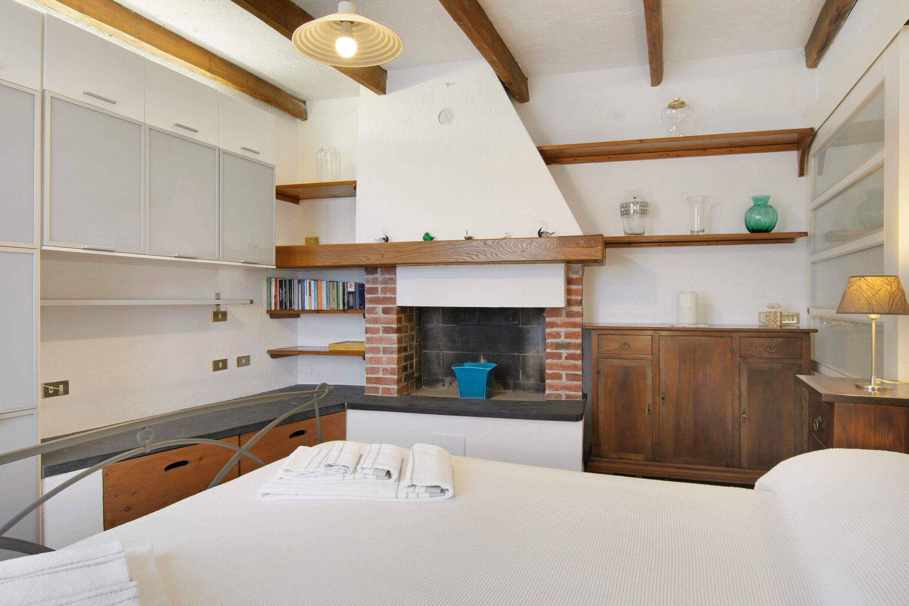 A bedroom with a bed, a bedside table, a dresser, a fireplace, and a window.