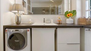 A compact bathroom with a washing machine, a sink, a mirror, and a vase with sunflowers.