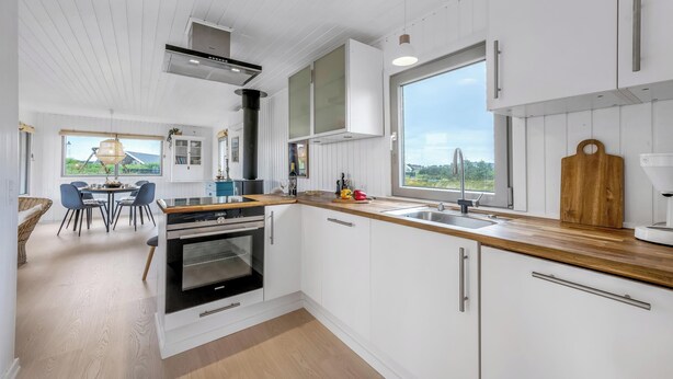 Une cuisine moderne avec des meubles blancs, un plan de travail en bois, une grande fenêtre et un coin repas avec des chaises.
