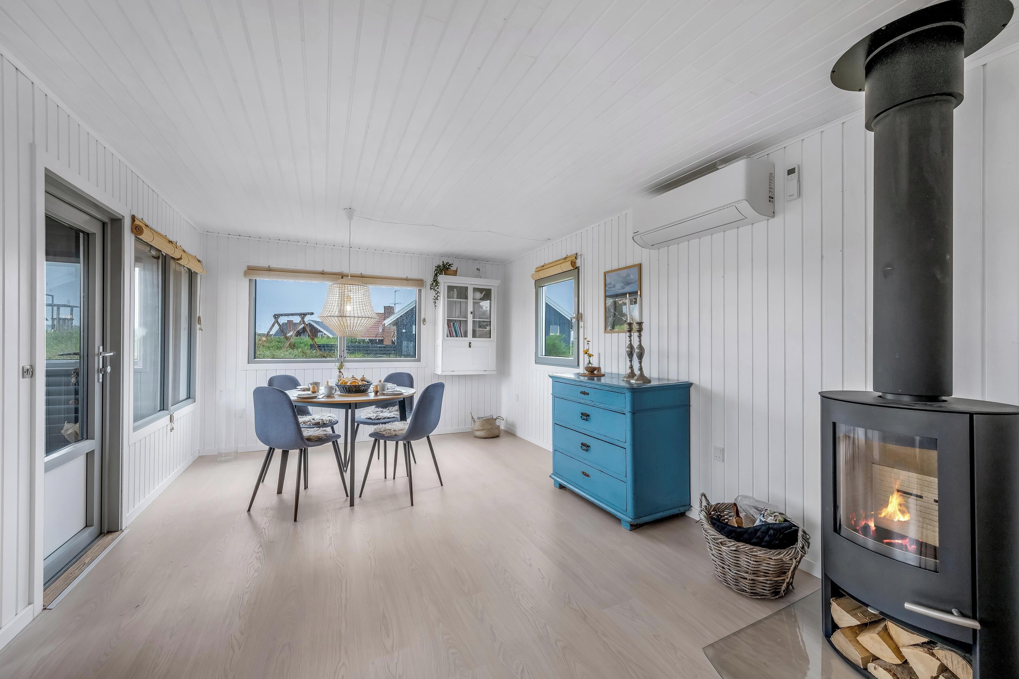 En modern inredning med ett matområde, en blå byrå, en vedeldad kamin och stora fönster.