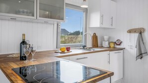 Une cuisine moderne dotée d’une plaque de cuisson en verre, de meubles blancs, d’une fenêtre et d’un plan de travail en bois.